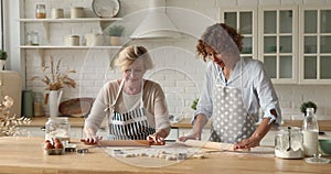 Cheerful woman her elderly mother making dough cooking in kitchen