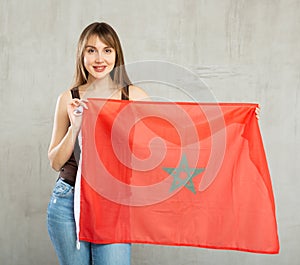 Cheerful woman holding flag of Morocco posing in studio
