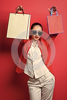 cheerful woman holding gift. portrait of an excited beautiful girl holding shopping bags over red background. woman