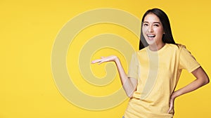Cheerful woman holding her hand with product or empty copy space while standing over isolated on yellow background