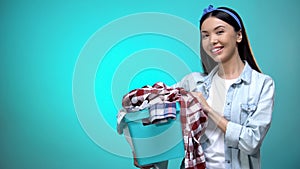 Cheerful woman holding laundry basket and smiling at camera, template for text
