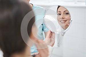 Cheerful woman looking in the mirror in cosmetology clinic