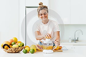 Cheerful woman with a lot of citrus fruits during fresh orange juice preparation at home