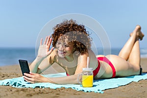 Cheerful woman lying on beach and making video call