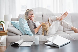 Cheerful woman lying on sofa cuddling a ginger cat