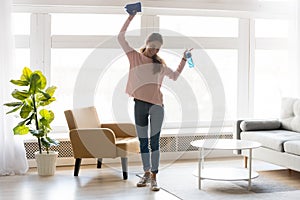 Cheerful woman makes house cleaning holding rag spray bottle detergent