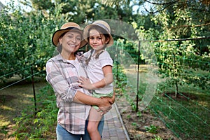 Cheerful woman, mom holding her little daughter on her arms, standing together in rows of seedlings in the organic farm