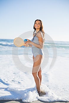 Cheerful woman in one piece swimsuit playing with beach racket