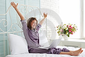 Cheerful woman in pajamas at the bedside with hands lifted and l photo