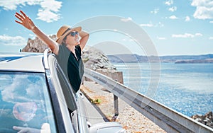 Cheerful Woman portrait enjoying the seaside road trip. Dressed a black dress, straw hat and sungllasses she wide opened arms and