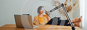 Cheerful  woman radio host sits with his feet up on his desk and recording audio podcast