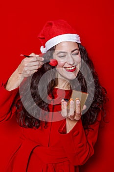 Cheerful woman in Santa hat putting on makeup