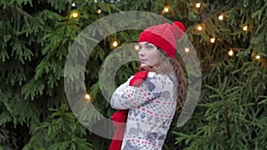 Cheerful woman in santa hat with red scarf and mittens is happy and jumping against the background of Christmas tree in