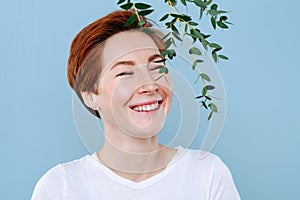 Cheerful woman with short ginger hair being tickled by an eucalyptus branch