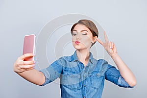 Cheerful woman showing v-sign while taking selfie on her smartp