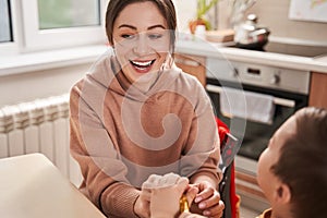 Cheerful woman sitting at the kitchen and playing with her little son