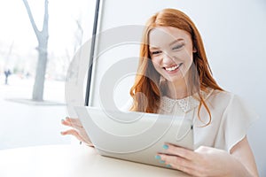 Cheerful woman smiling and using tablet in cafe
