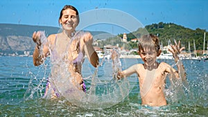 Cheerful woman with son enjoying summer beach vacation splashing sea water