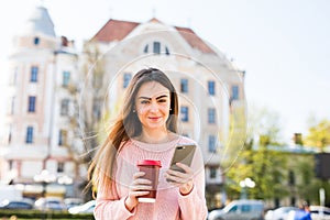 Cheerful woman in the street drinking morning coffee and use her smartphone. Woman texting