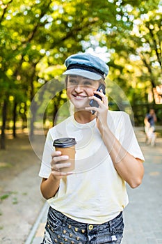 Cheerful woman talking phone and holding a paper cup on the street