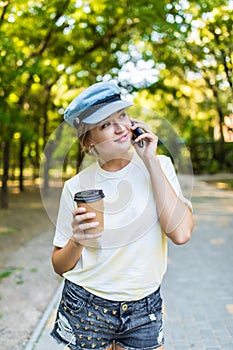 Cheerful woman talking phone and holding a paper cup on the street