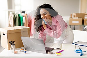 Cheerful Woman Talking On Phone Using Laptop In Clothing Store