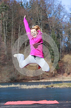 Cheerful woman teenage girl in pink tracksuit jumping outdoor