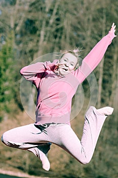 Cheerful woman teenage girl in pink tracksuit jumping outdoor