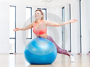 Cheerful woman training with fitball at fitness club.