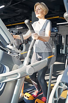 Cheerful woman using cardio stepper machine in gym