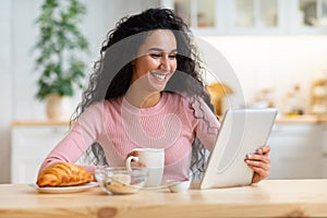 Cheerful Woman Using Digital Tablet While Having Breakfast In Kitchen At Home