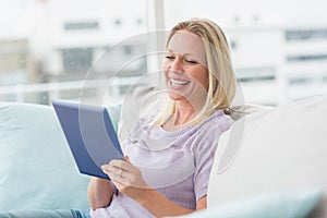 Cheerful woman using tablet computer on sofa