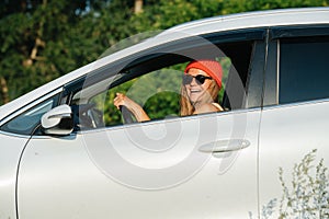 Cheerful woman in a watch cap driving in a countryside, holding coffee cup photo