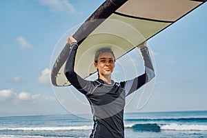 Cheerful woman in wetsuit holding surfboard on beach