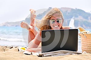 Cheerful woman is working on laptop on beach