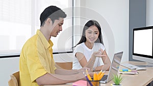 Cheerful woman working on their start up project with her colleague at bright modern office.