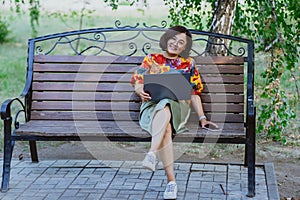 Cheerful woman works on her laptop while sitting on park bench