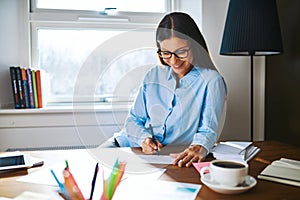 Cheerful woman writing checks at desk