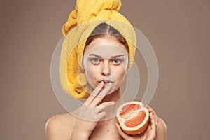 cheerful woman with a yellow towel on her head bare shoulders grapefruit in hand natural cosmetics