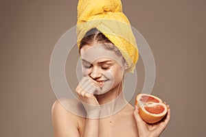 Cheerful woman with a yellow towel on her head bare shoulders grapefruit in hand natural cosmetics