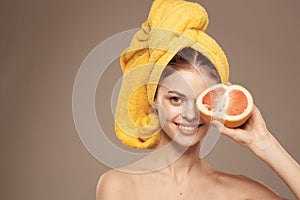 Cheerful woman with a yellow towel on her head bare shoulders grapefruit in hand natural cosmetics