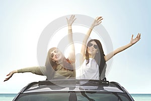 Cheerful women enjoying freedom on car sunroof