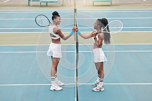 Cheerful women holding hands over the net on a tennis court. Young women support each other after tennis practice