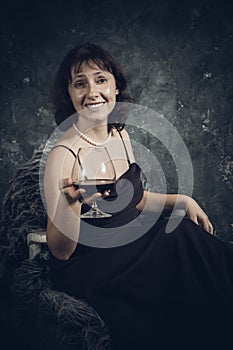 Cheerful 40 years old woman in classic dress with glass of wine