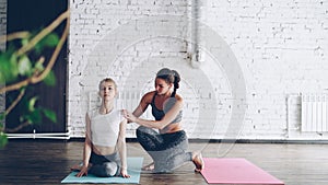 Cheerful yoga teacher is helping new student master cow face pose during one-to-one class in modern sports center. Women