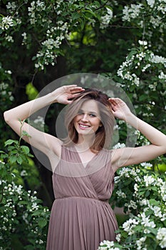 Cheerful young adult woman female model with clean fresh skin, make-up and brown hair in blossom garden on green leaves background