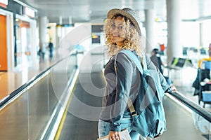 Cheerful young adult woman travel at the airport with backpack. Female people portrait smiling and walking at the gate. Pretty