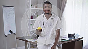 Cheerful young African American doctor juggling lemon smiling looking at camera. Portrait of confident expert man posing