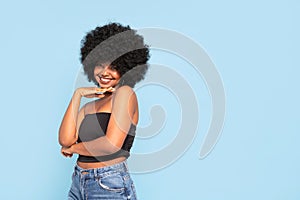 Cheerful young African American female model in black top and jeans, with afro hairstyle, smiling to the camera. Real people