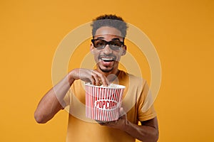 Cheerful young african american guy in 3d imax glasses posing isolated on yellow orange background in studio. People